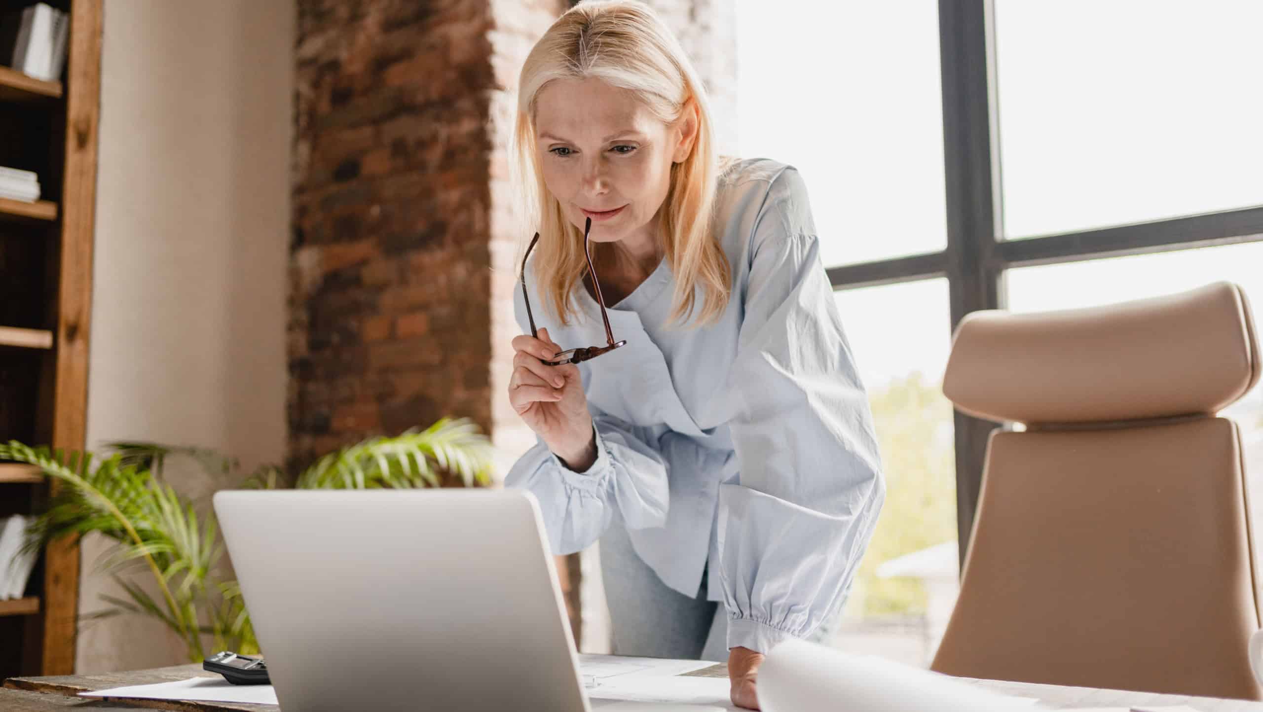 Concentrated caucasian middle-aged mature businesswoman ceo boss typing on laptop, working at office desk with documents, searching surfing web online