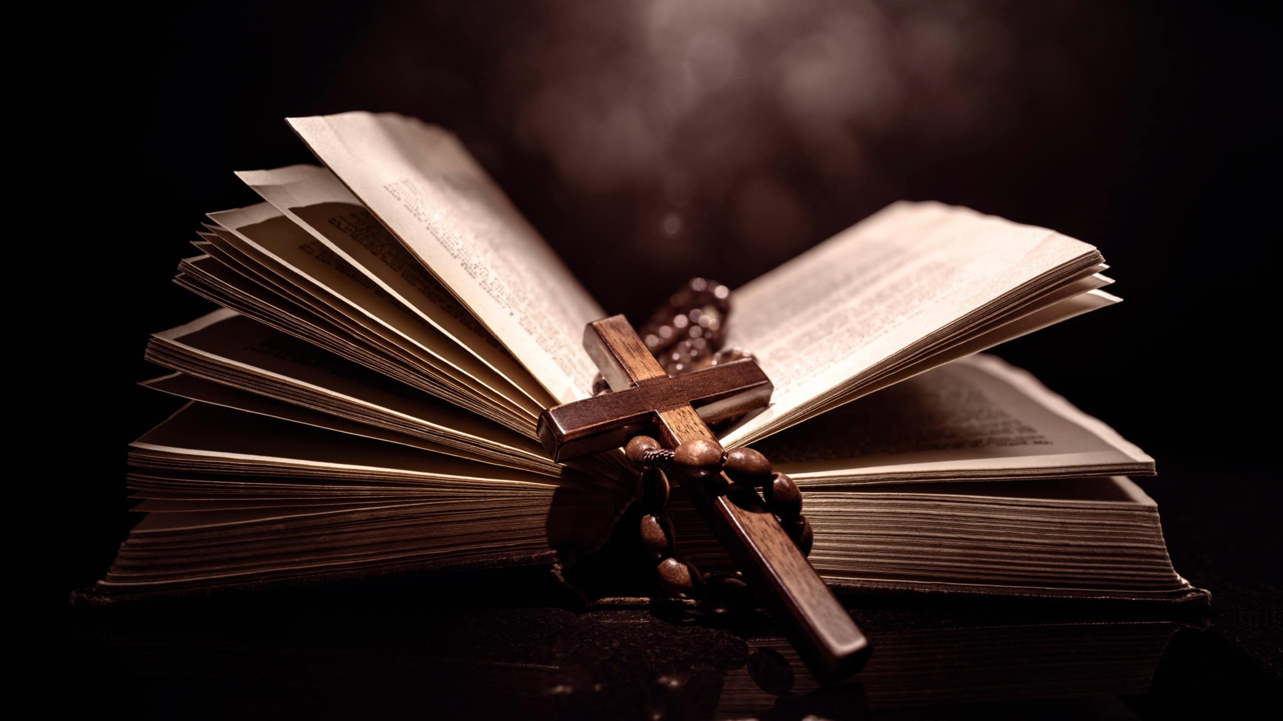 Praying with wooden crucifix cross on Holy Bible study background