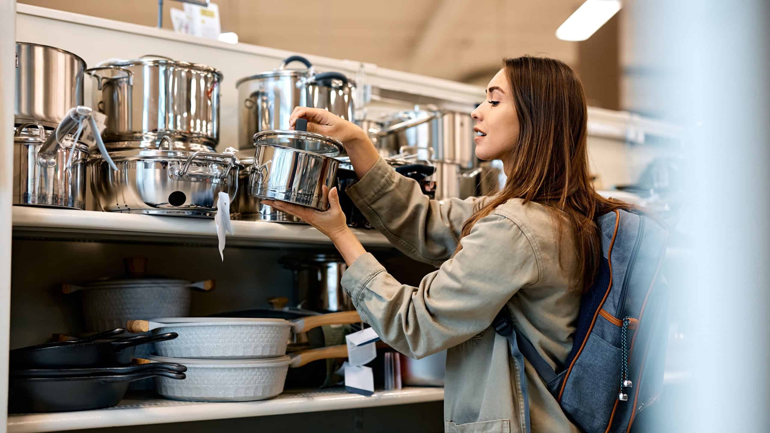 Young happy woman buying new cooking pot in the supermarket