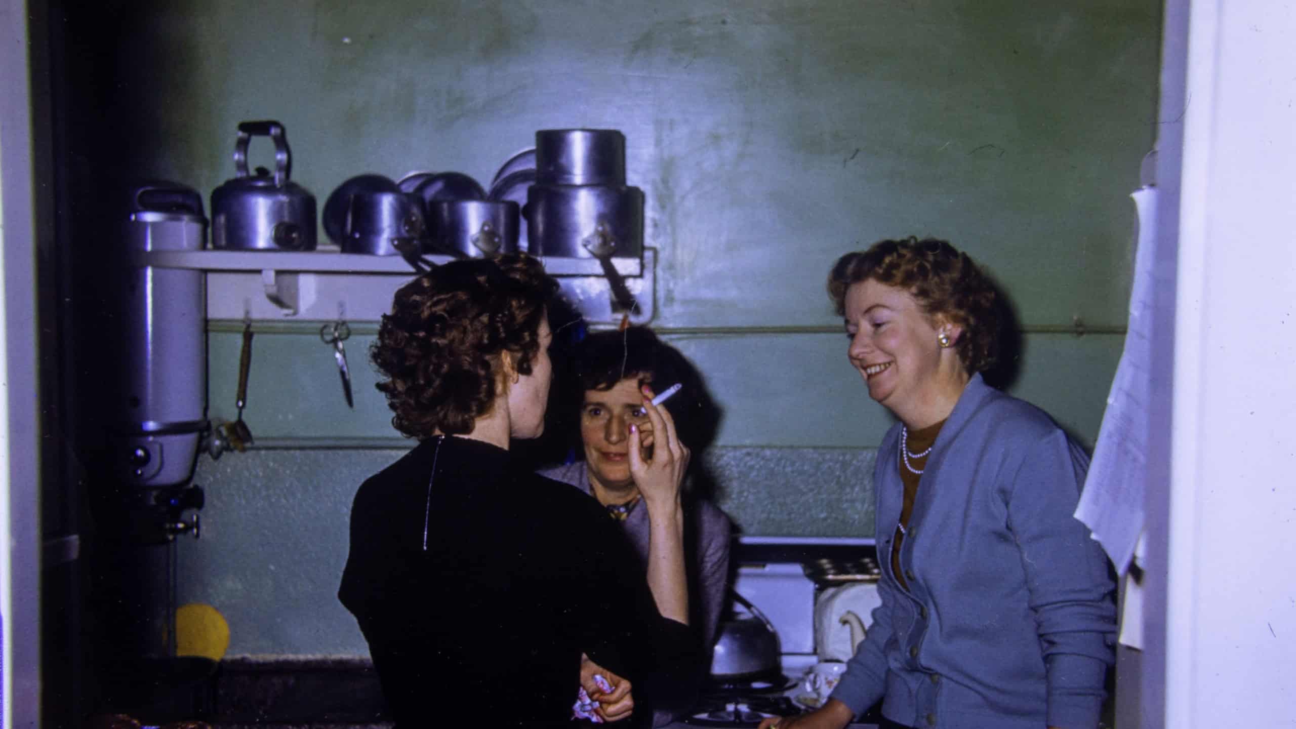 London UK, 21st December 1953:An extremely old vintage photo from 1959 showing a British kitchen with women and house wives chatting and talking while smoking a cigarette