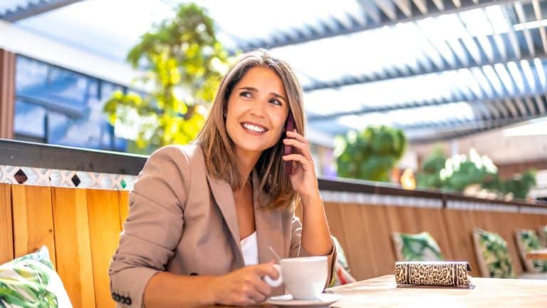 Happy mature woman drinking coffee and talking to the phone sitting on a cafeteria