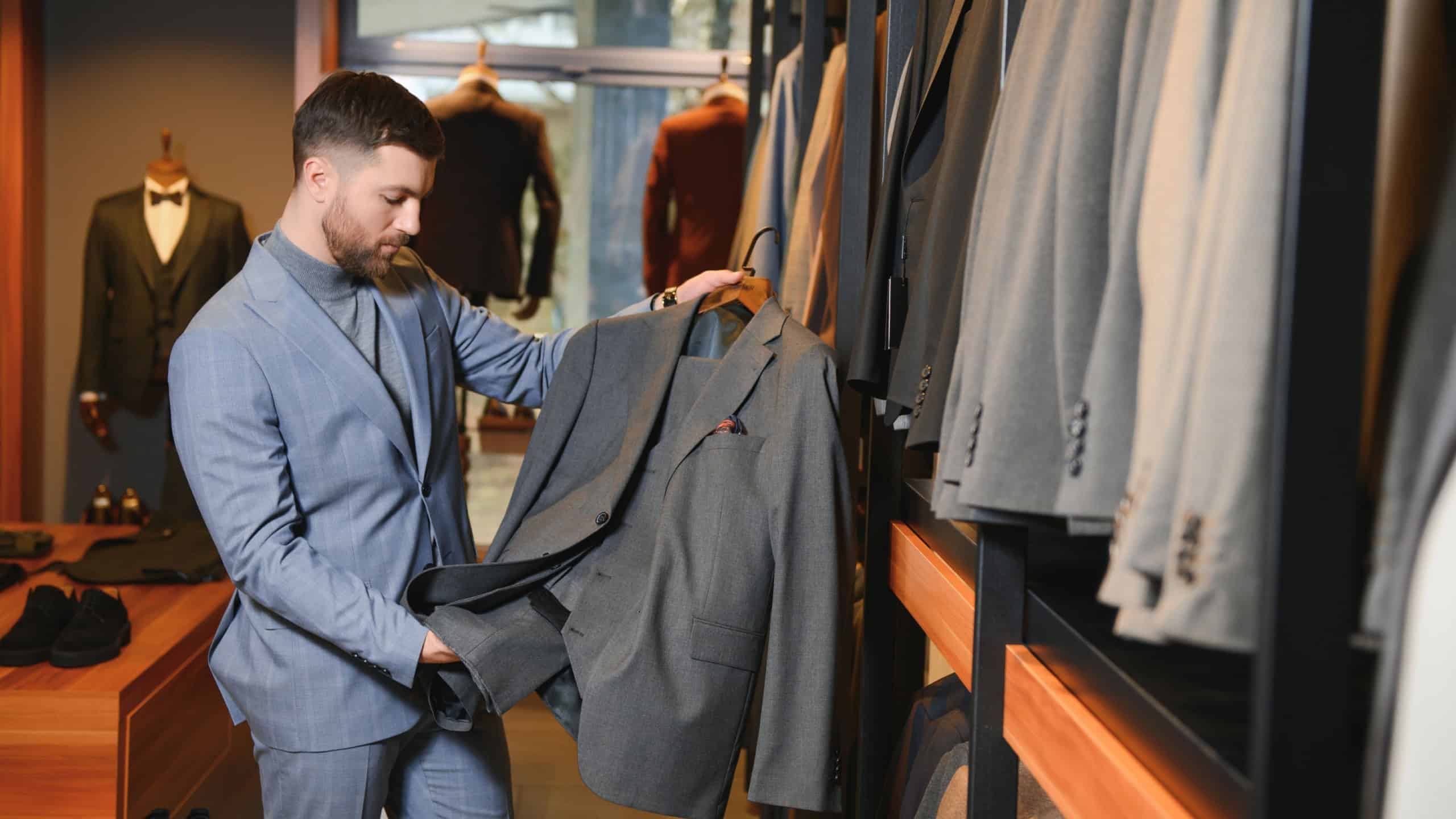 Businessman in classic vest against row of suits in shop.
