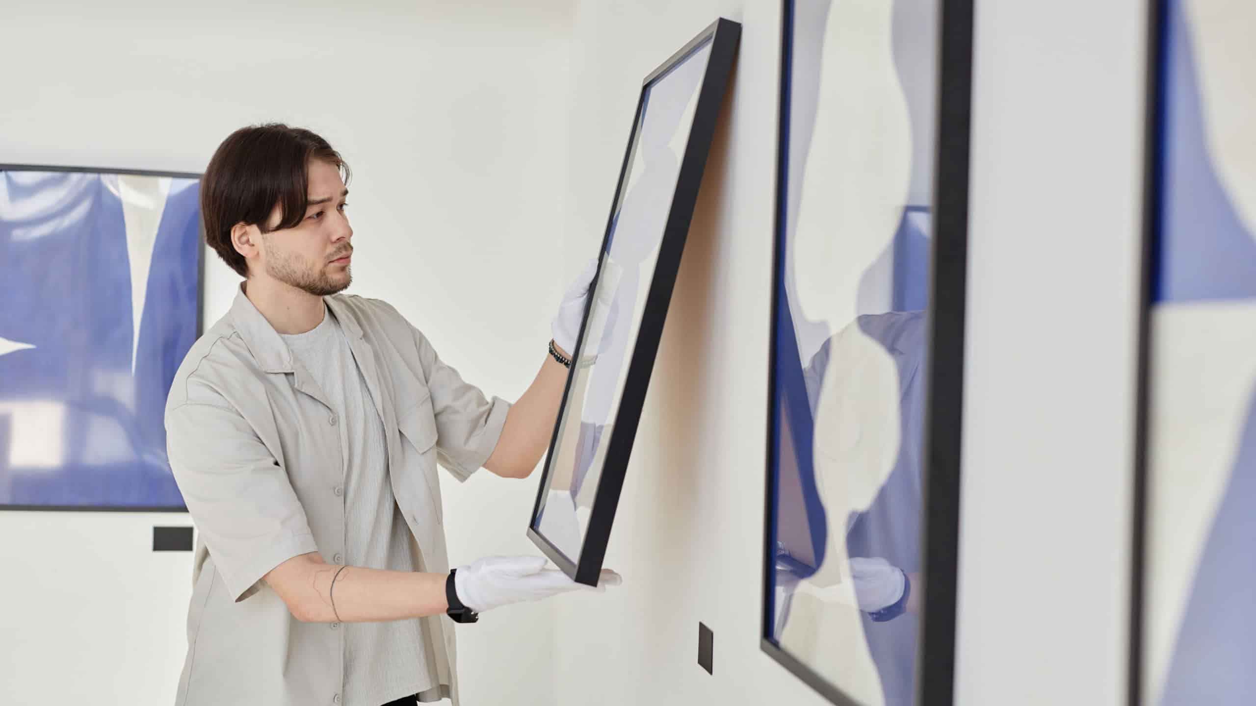 Minimal side view portrait of young Asian man working as art curator and hanging paintings on wall while planning modern art gallery exhibition
