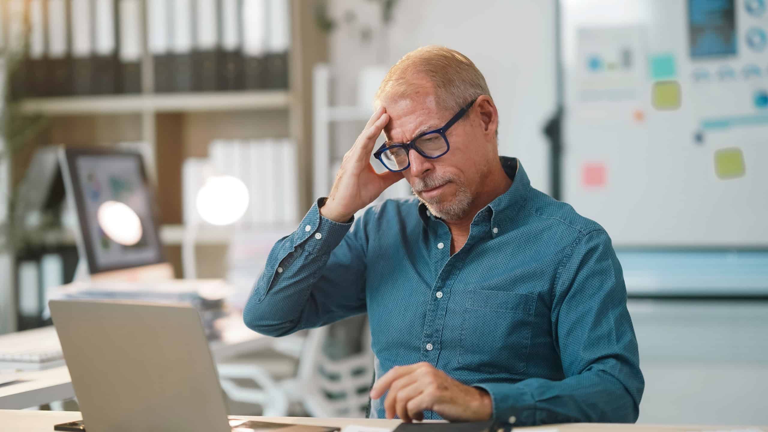 Senior businessman experiencing a headache while working at his desk, touching his head with his hand