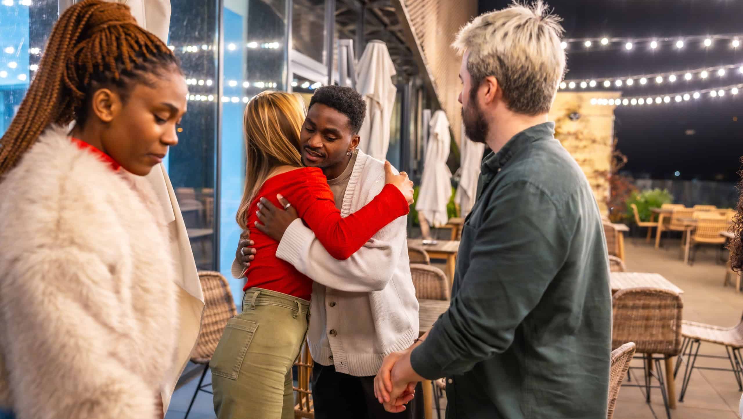 Multiracial friends saying goodbye after a dinner on a terrace at night