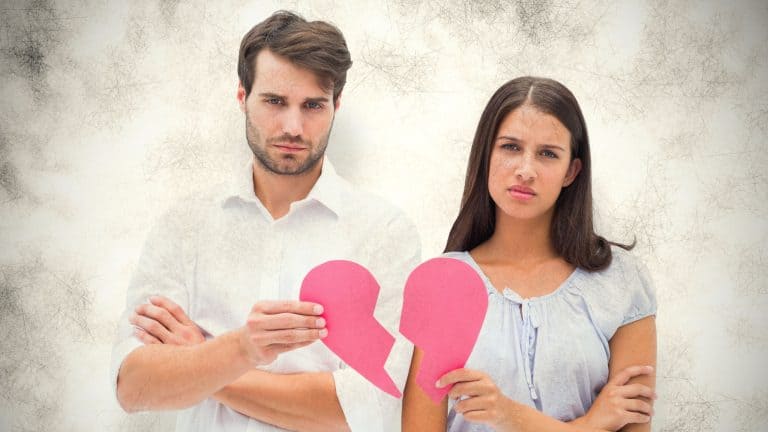 Upset couple holding two halves of broken heart against grey background