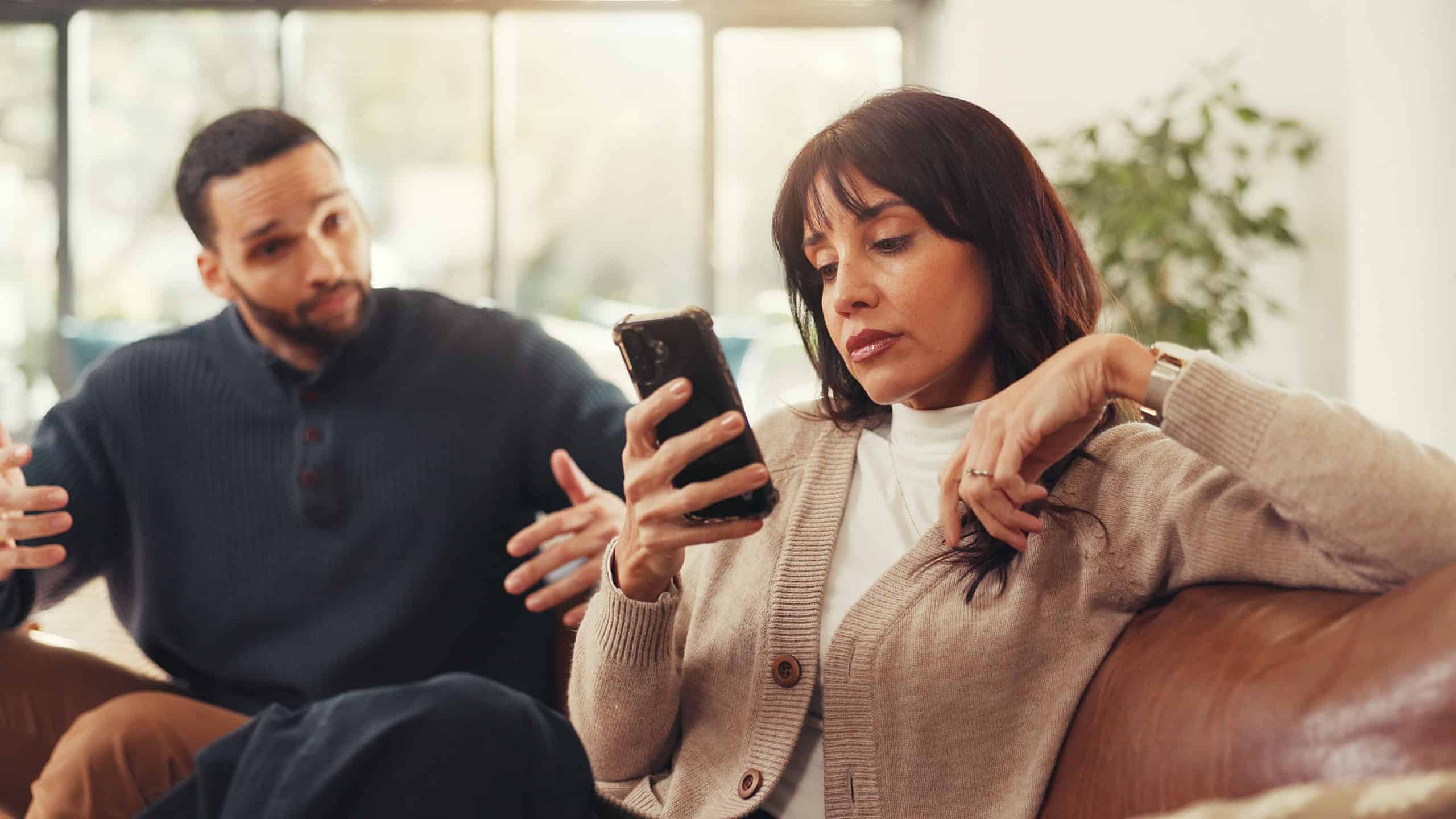 Woman, phone and ignore man on couch with social media addiction, talk and gesture for attention. Person, couple and smartphone with distraction, game or web chat with mobile app in lounge at house