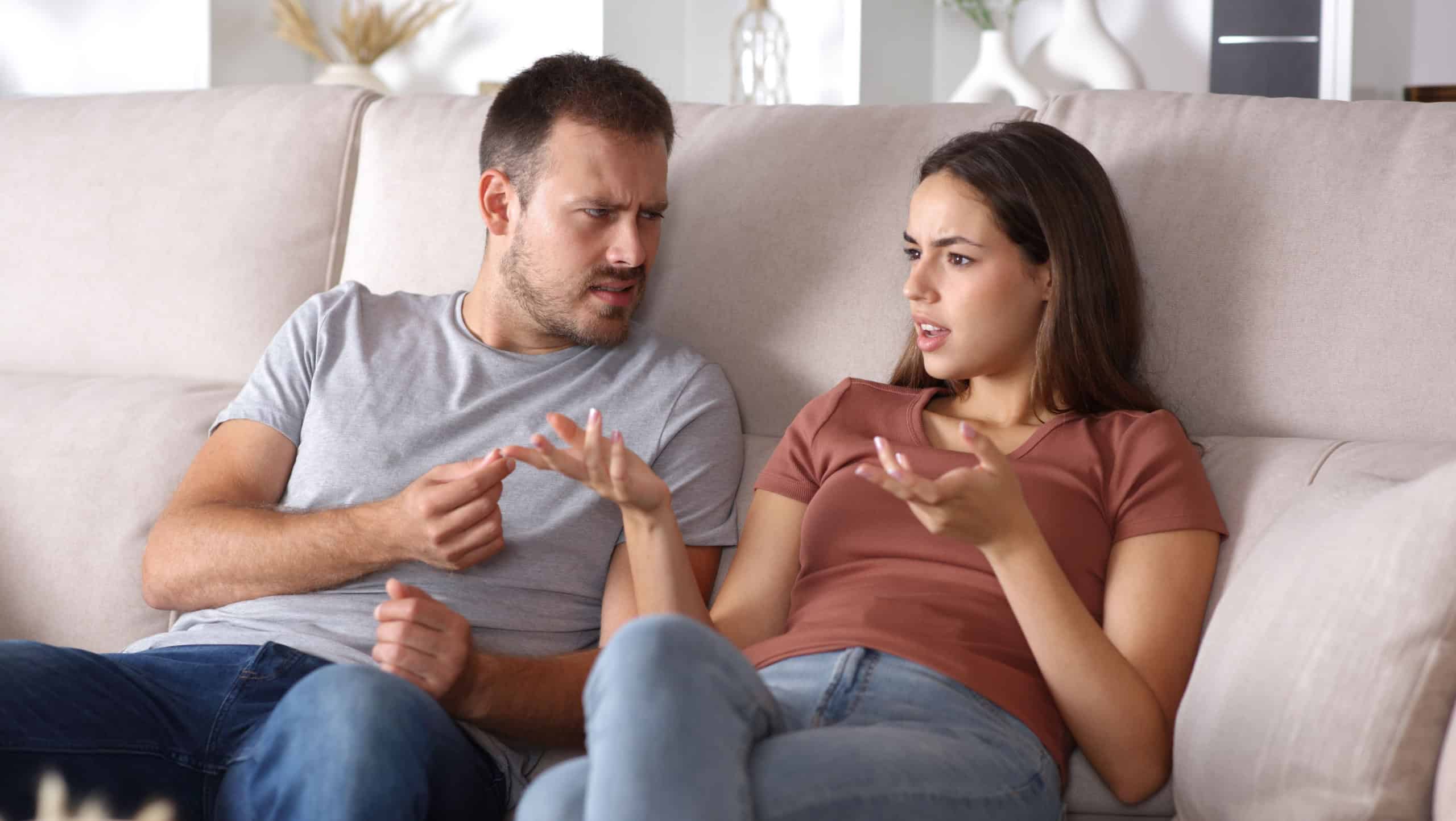 Couple talking and disagreeing sitting on a sofa at home