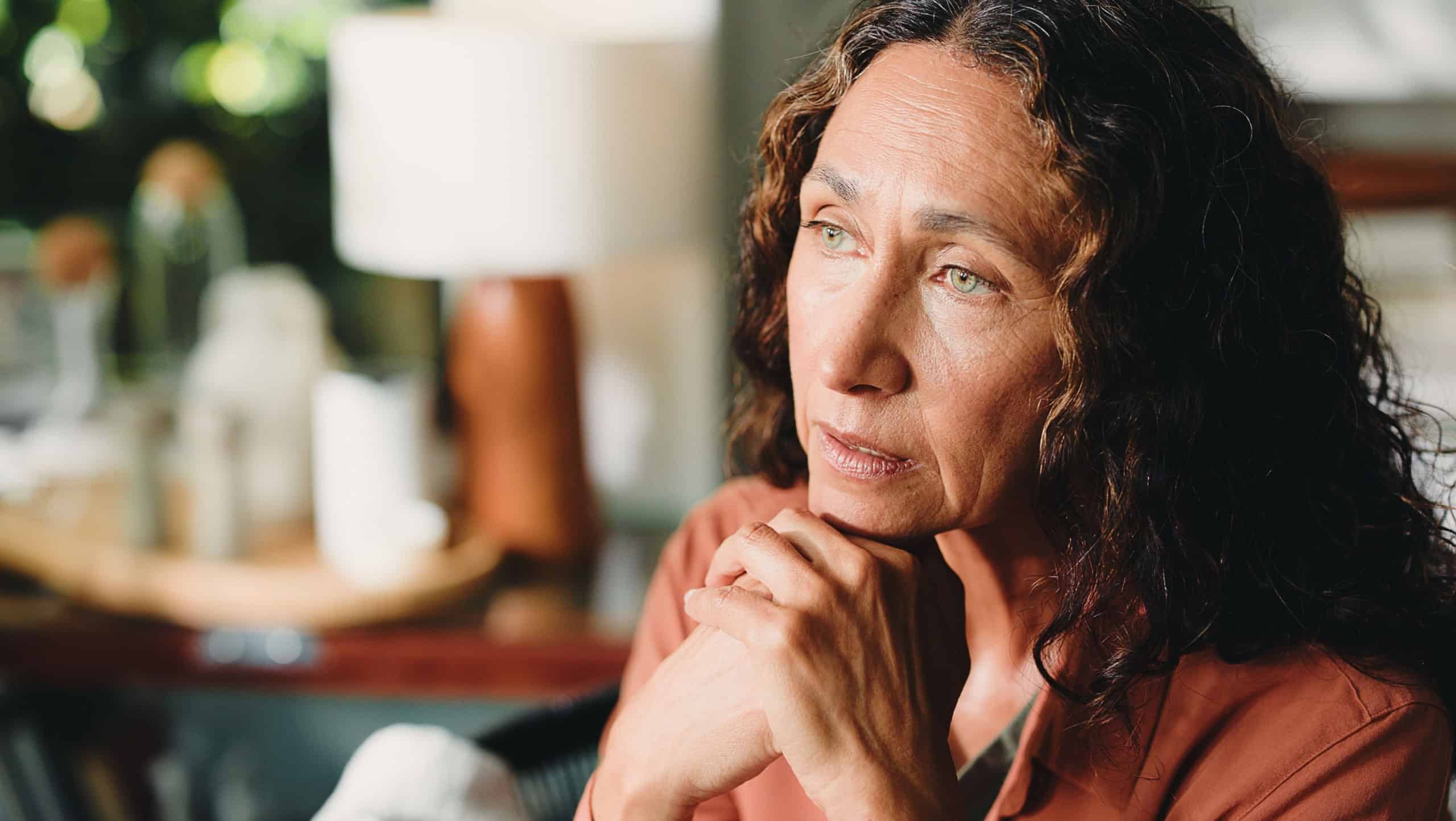 Reflection, nostalgia and mature woman in house with thoughts, past memory and sadness in living room. Mindset, space or senior person in home with perspective, wondering and loss in flashback.