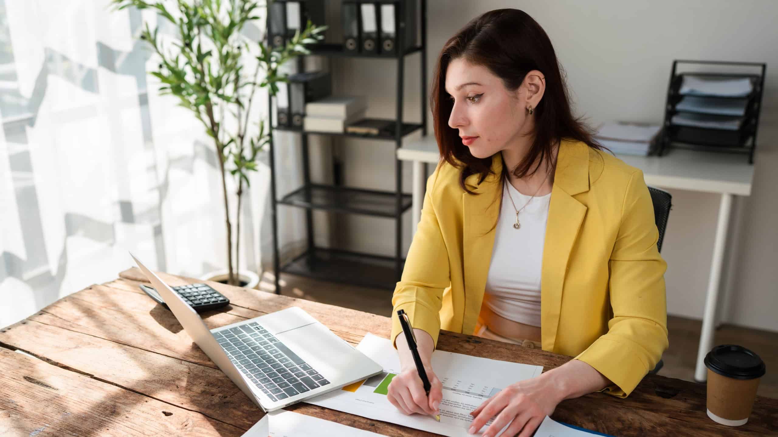 Young woman working at a desk, reviewing charts and writing notes for business planning