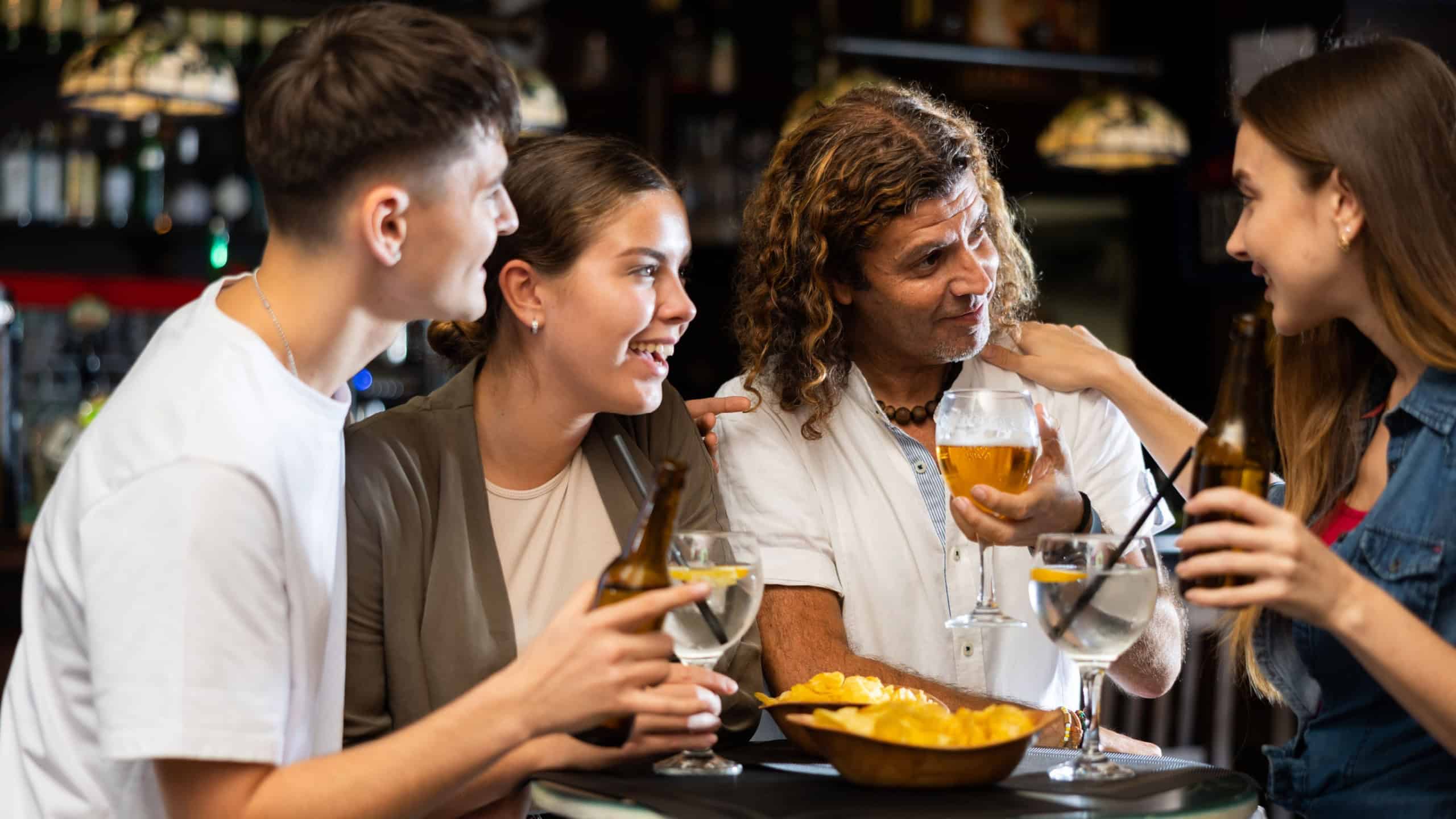 Positive men and women drinking beer and chatting in bar. Friends meeting in pub.