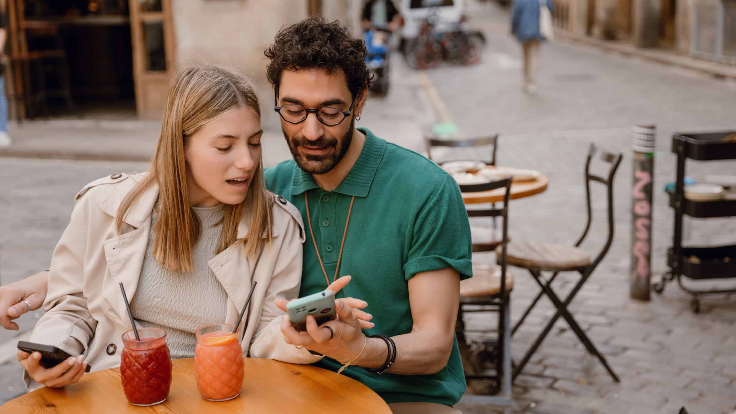 A man and a woman are sitting at a table and looking at the phone he is showing while they are talking