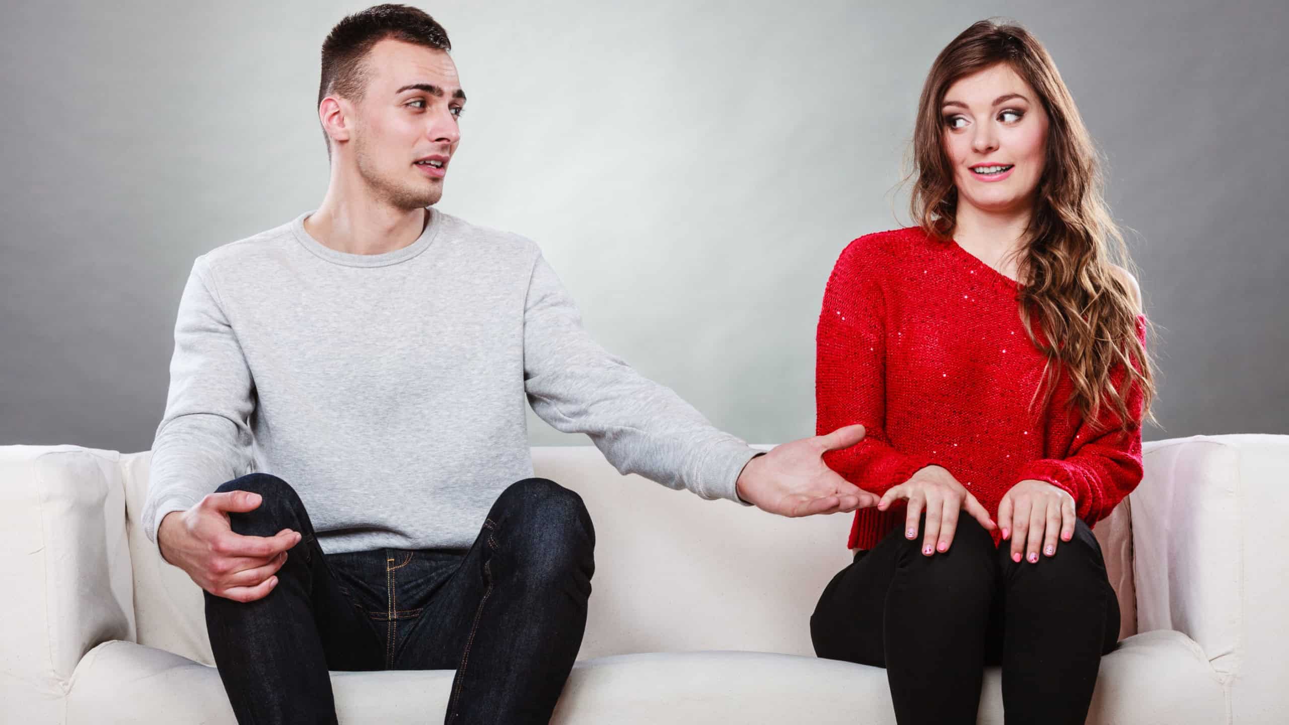 Shy woman and man sitting on sofa couch next each other. First date. Attractive girl and handsome guy meeting dating and trying to talk. Male offering a hand to female.