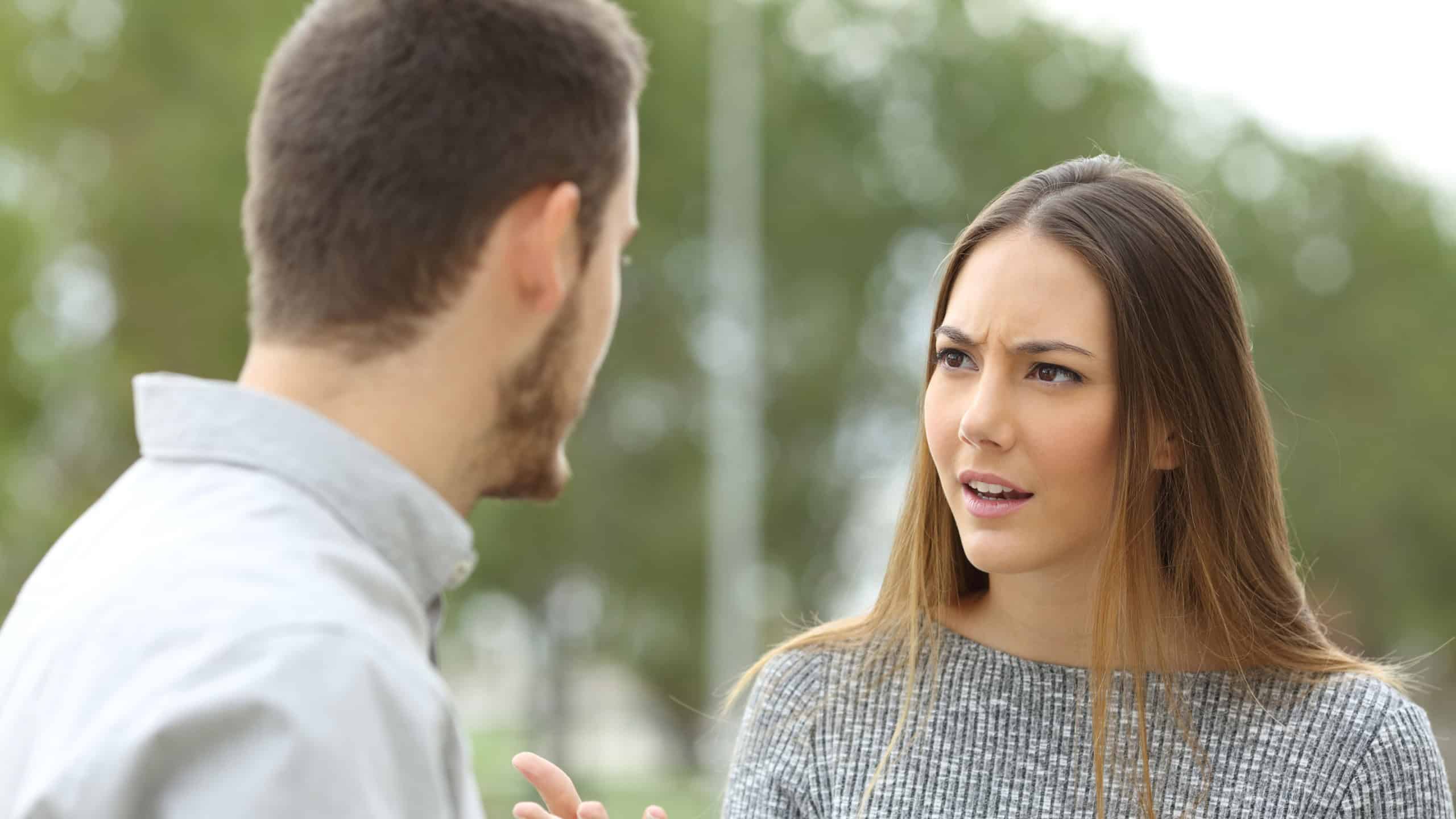 Couple talking seriously outdoors in a park with a green background