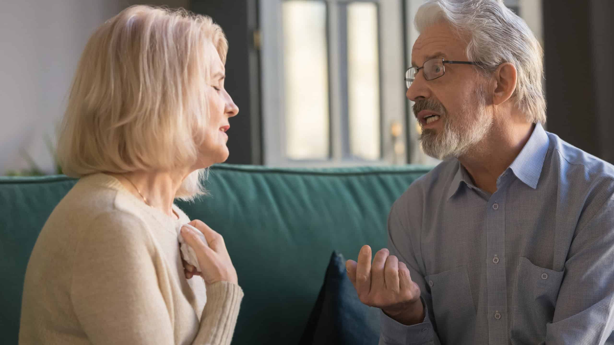 Senior husband and wife sit on couch at home talk dispute on family relations problem, stubborn mature couple having disagreement misunderstanding speak discuss health troubles or relationships