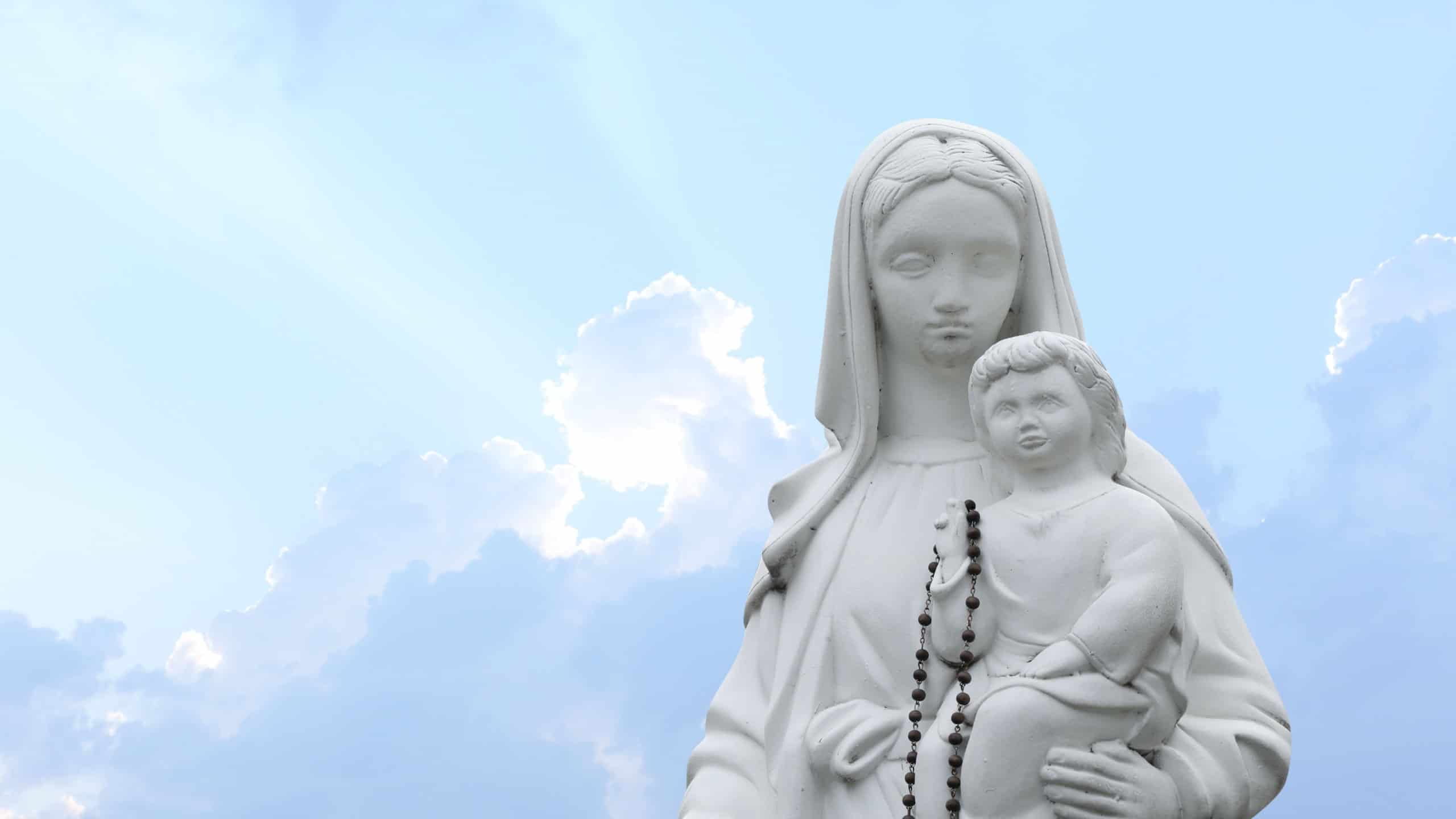 Beautiful statue of Virgin Mary and baby Jesus with rosary beads outdoors.