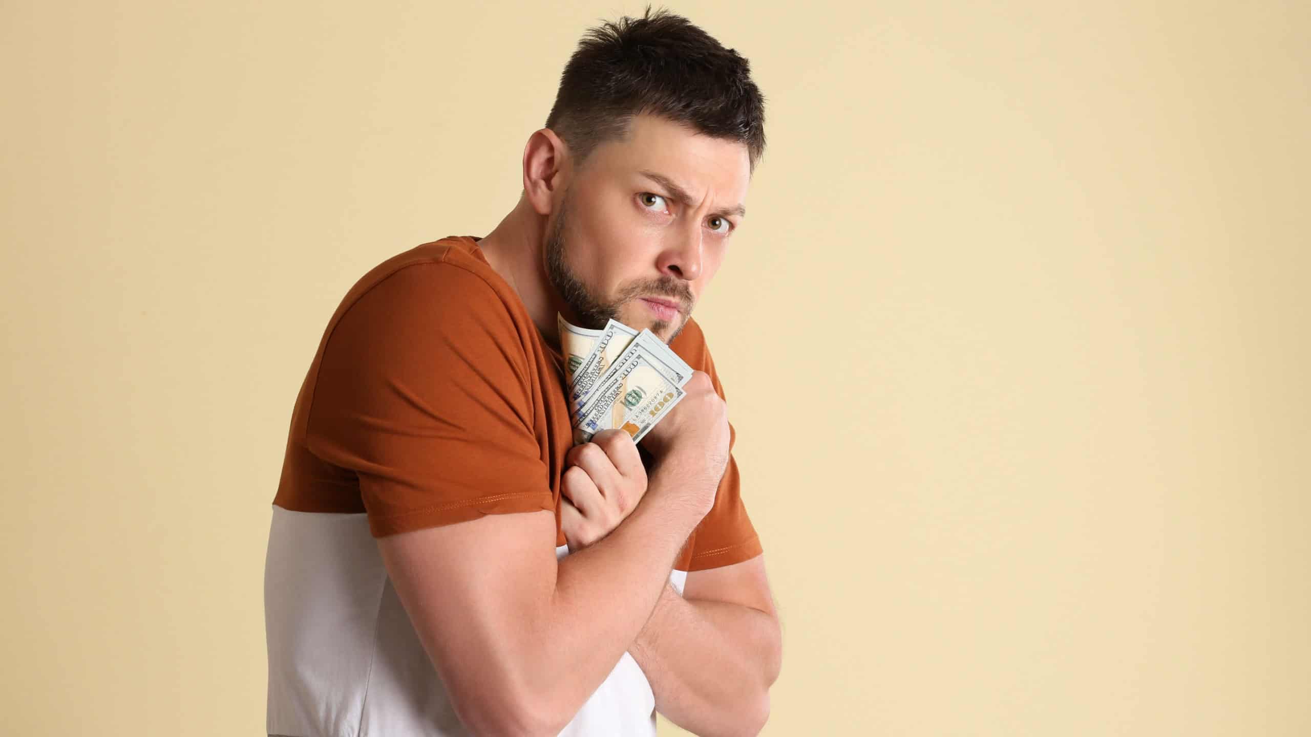 Greedy man hiding money on beige background.
