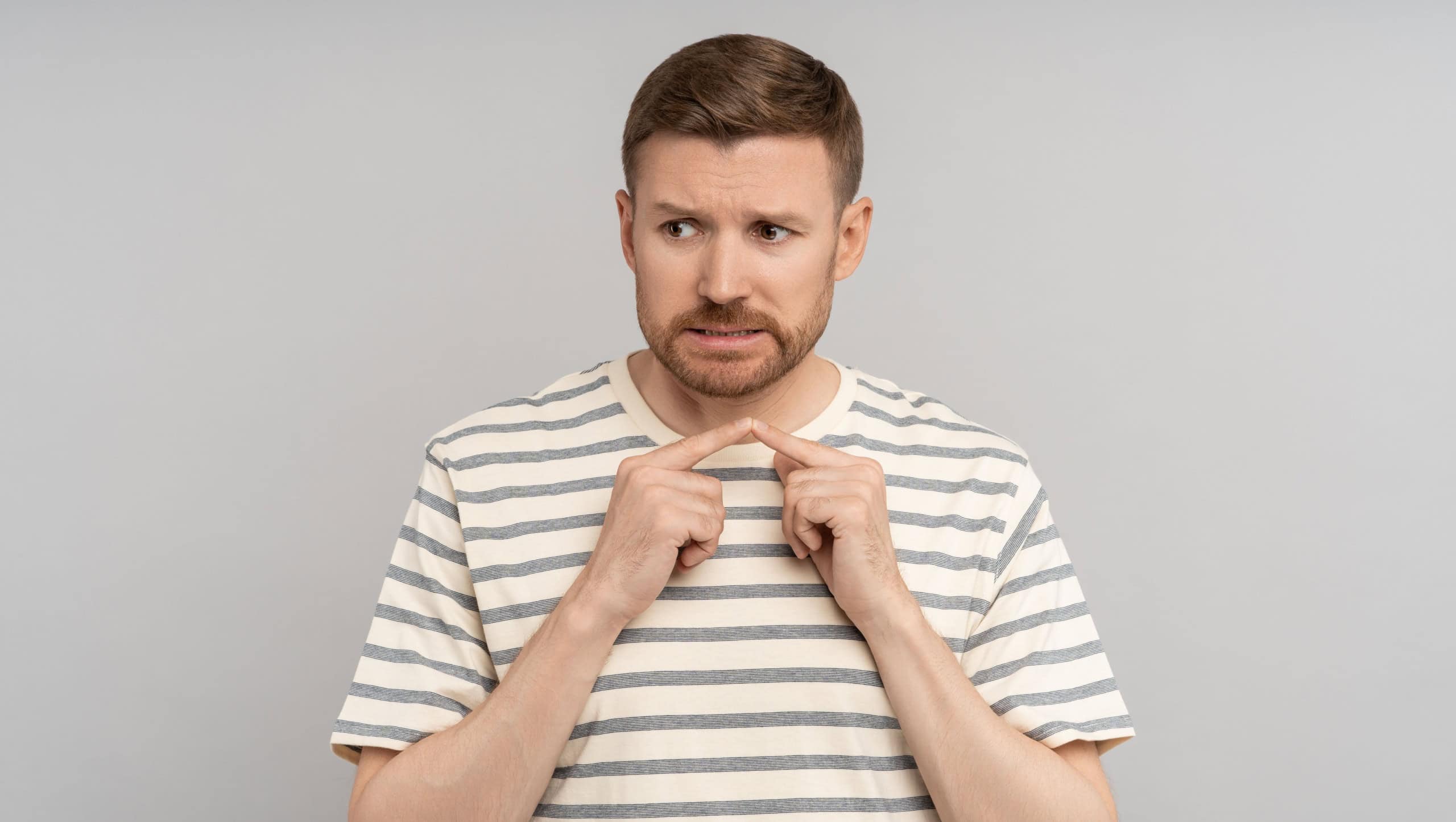 Nervous man connects his index fingers. Guy suffers from anxiety, uncertainty and doubts. Difficulties in making decision, indecision of Caucasian male, shyness awkwardness isolated on gray background