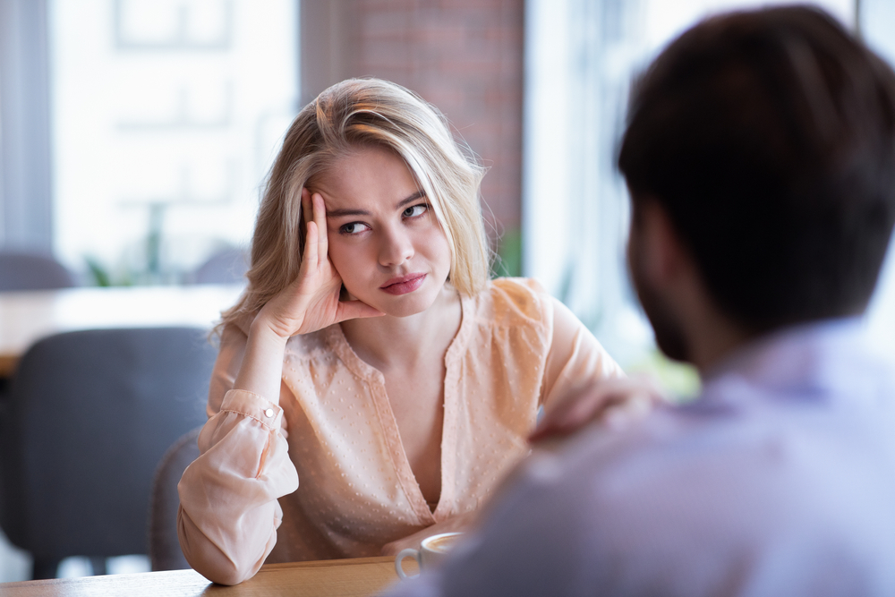 Young Caucasian woman disinterested in blind date, feeling bored with conversation at city cafe. Millennial couple having relationship problems, going through breakup or divorce