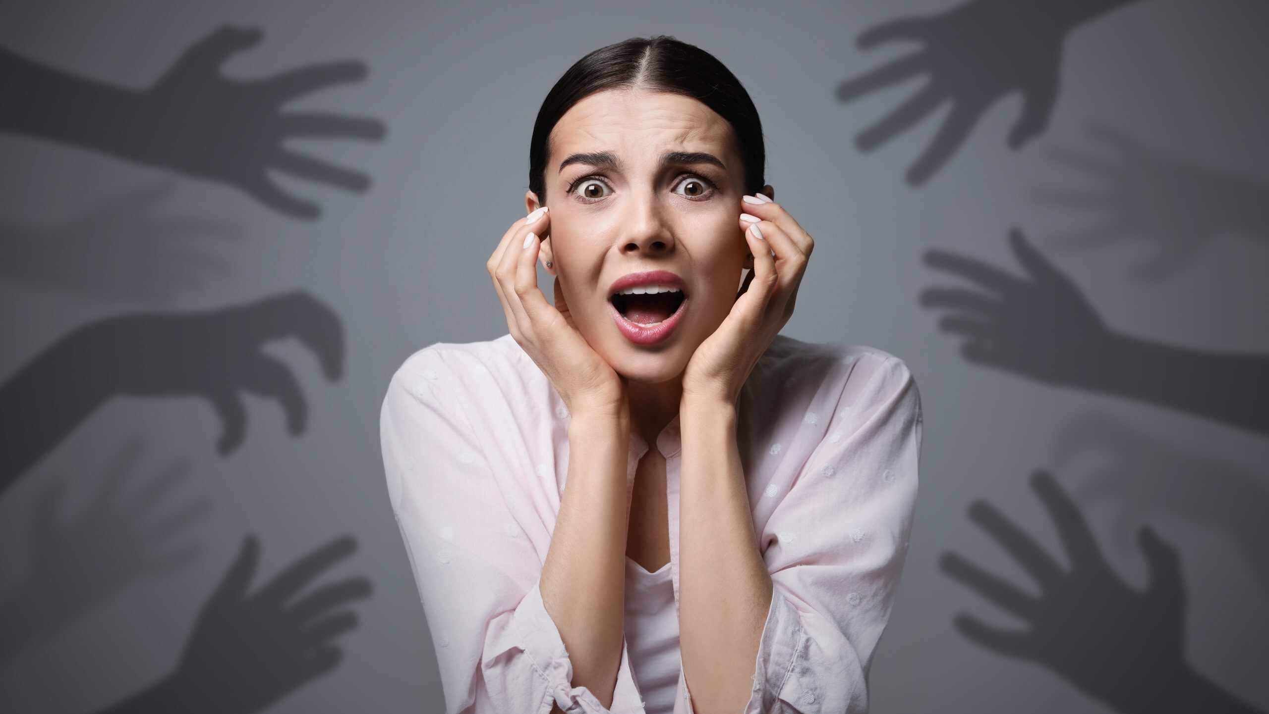 Paranoid delusion. Scared woman screaming on grey background. Shadows of hands reaching for her symbolizing fear and anxiety