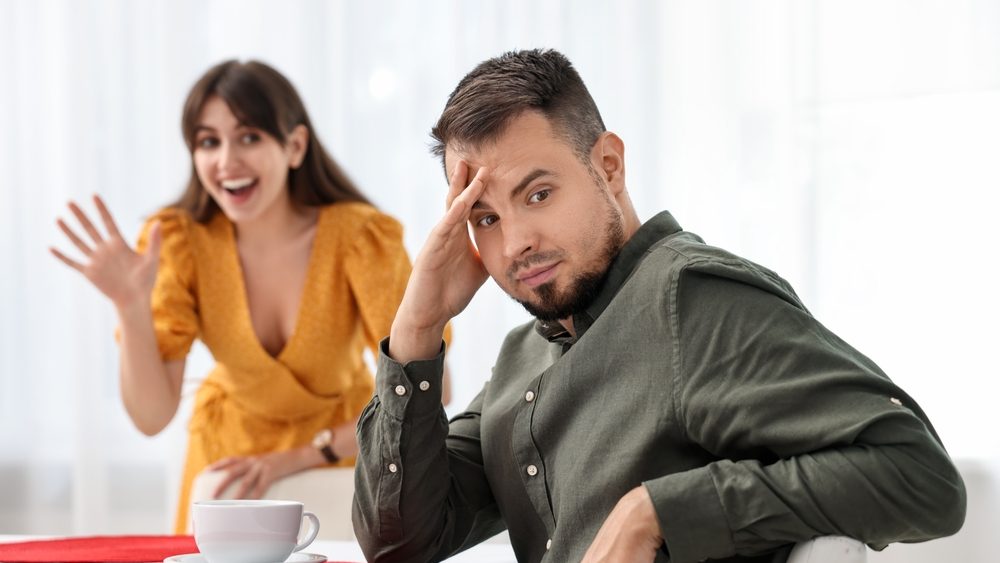 Bad date. Embarrassed man ignoring smiling woman indoors, selective focus
