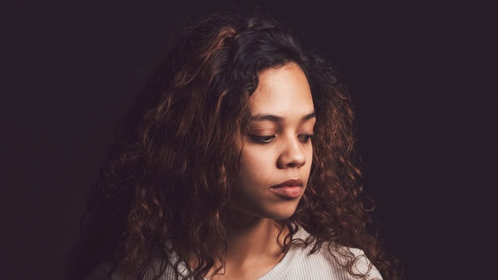 Sad, thinking and person with bipolar disorder in studio for mental health, psychology and ptsd illness. Identity crisis, mindset and depression with woman on black background for mood swing mockup