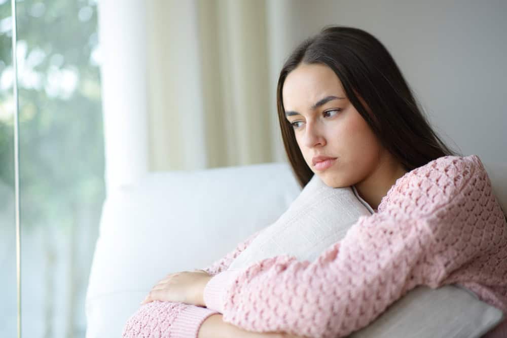 Angry pensive woman looks away through a window sitting on a couch at home