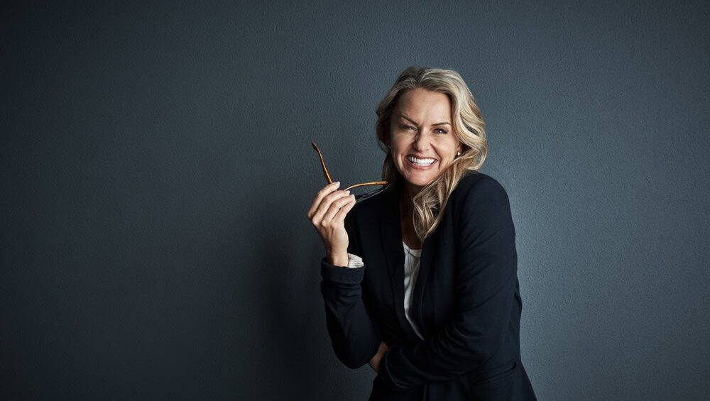 Glasses, laugh and portrait of business woman in studio for fashion designer, about us and confidence. Creative director, tailor and stylist vision with mature person on dark background for joke