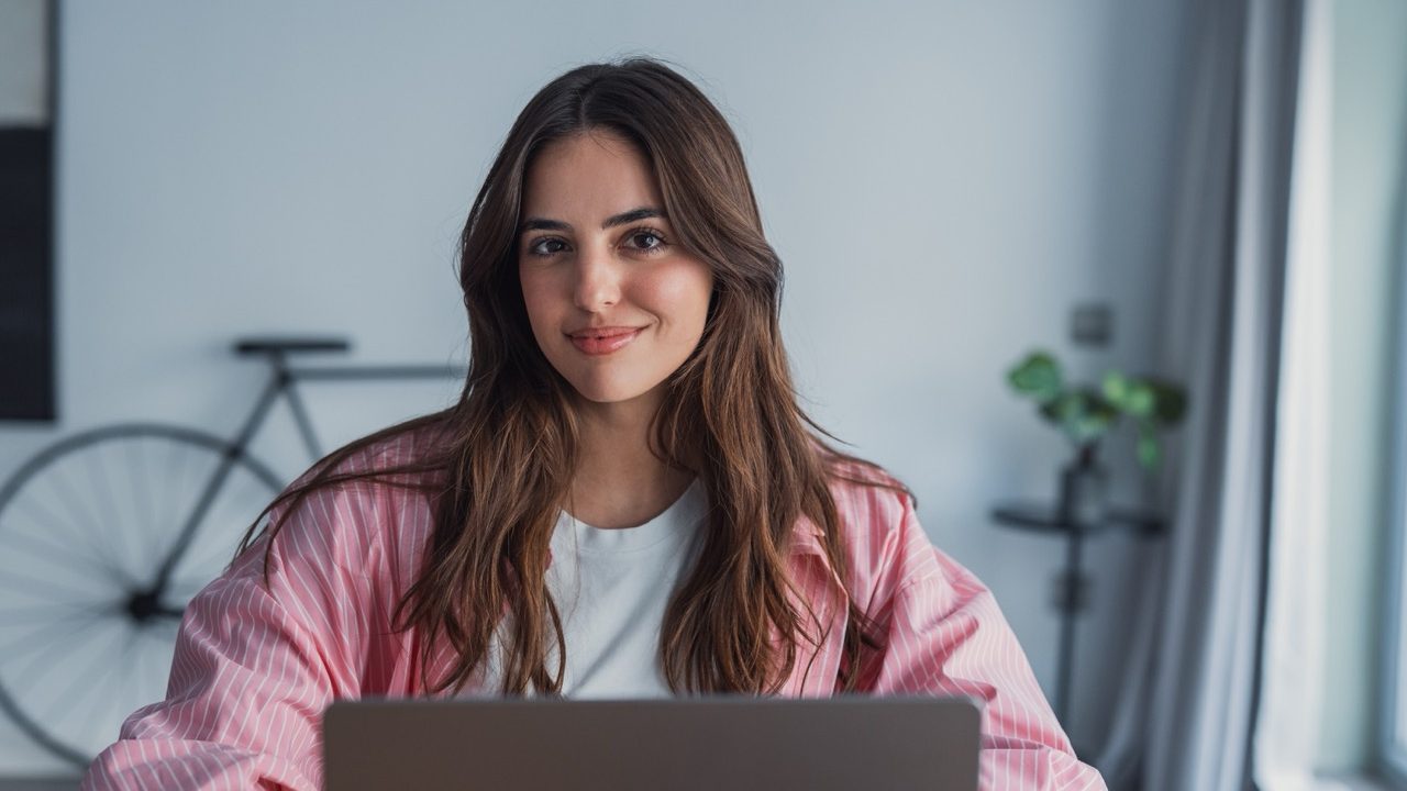 Happy young woman sit at desk look at laptop screen browsing surfing wireless Internet at home, smiling millennial female employee work on modern computer in living room, technology concept