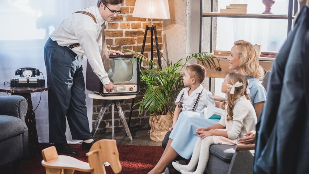 happy mother with two children looking at father turning on vintage tv, 50s style