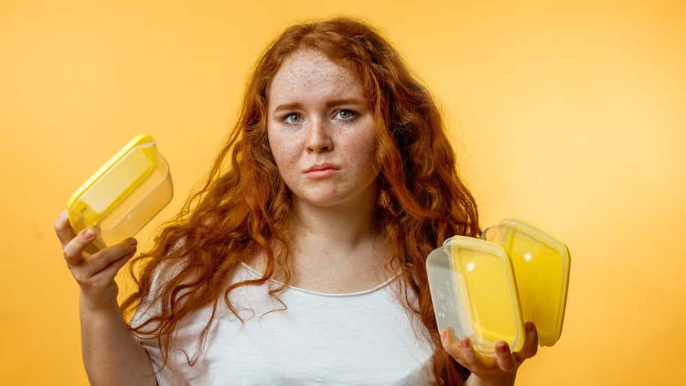 Displeased hungry plump woman holding empty lunch boxes and looking at it with offenced look. Healthy lifestyle, diet and people concept.