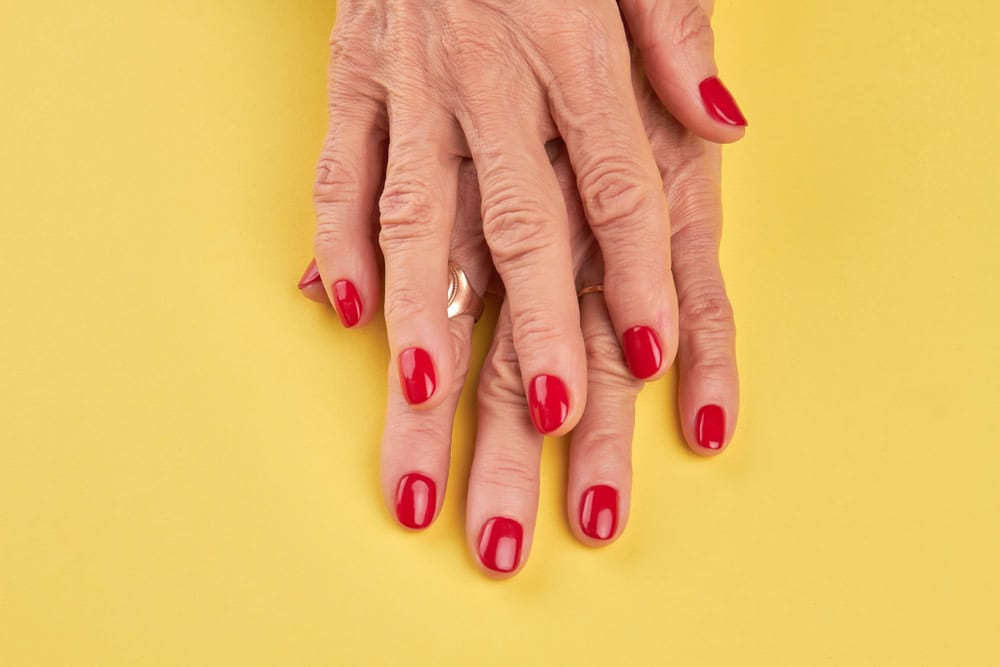Senior woman hands with perfect red manicure. Old woman well-groomed hands isolated on yellow background. Salon beauty and spa.