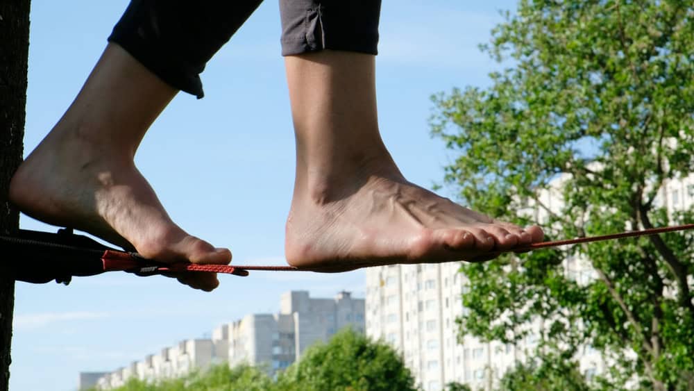 Woman legs walk along a tight line in a city park. Foot woman balances on the slackline side