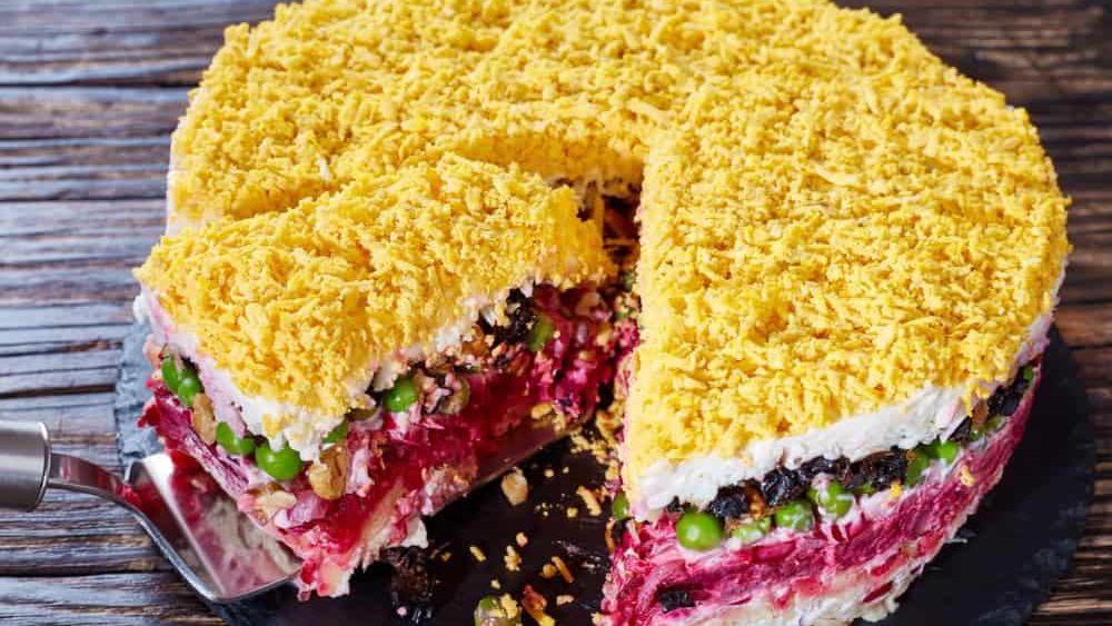 delicious seven layered salad with vegetables, hard boiled eggs, prunes, nuts and chicken meat on a black slate tray on an old wooden table. view from above, close-up