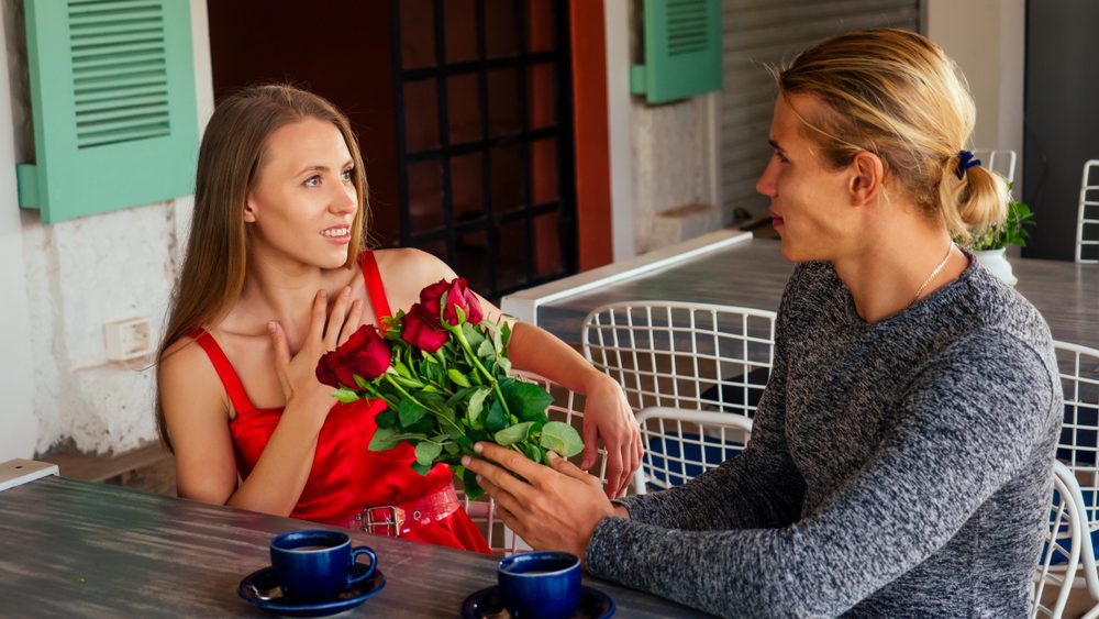 surprised blonde woman and handsome blond man at restaurant.happy couple romantic date, celebrating valentine day male model give red rose to his girl
