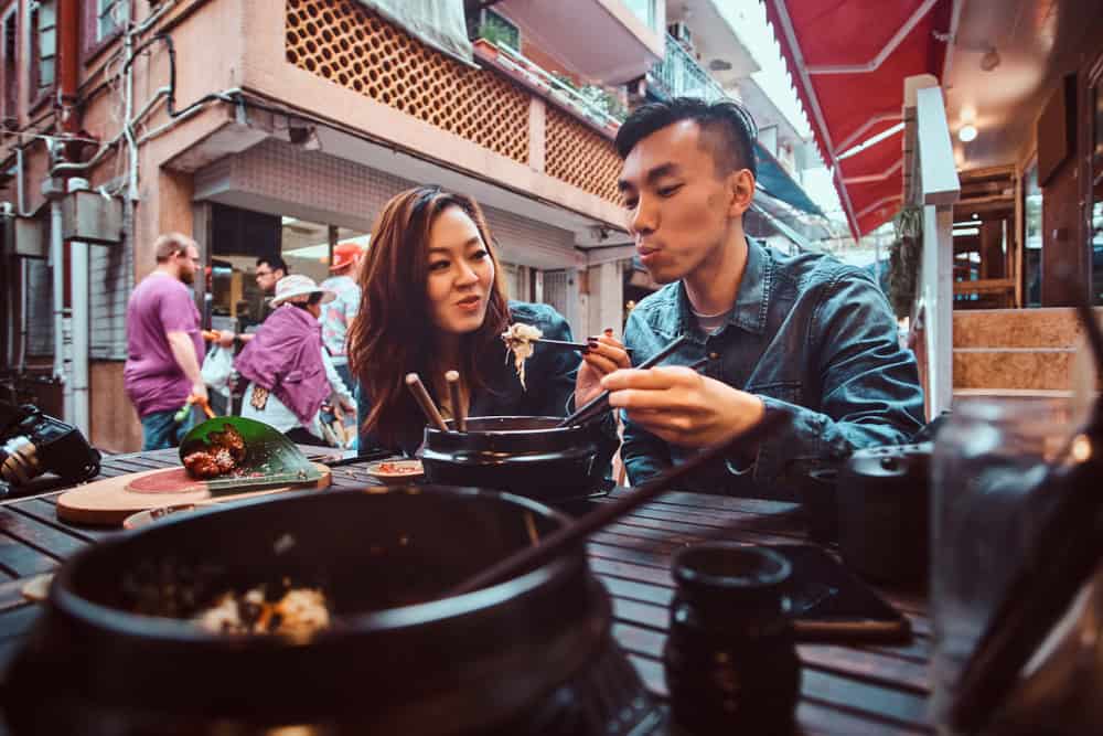 Smiling young chinese couple sitting at restourant outside and trying traditional asian food at first time. Widescreen shooting.