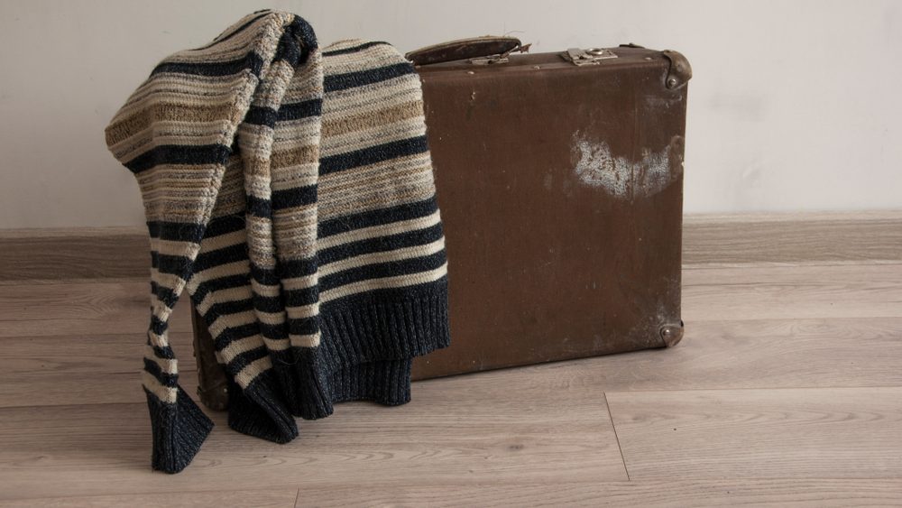 Men sweater on old travel suitcase in a room with a white wall