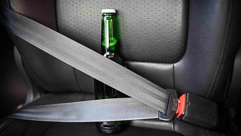 Bottle of alcohol fastened with seat belts. Drink and drive. Bottle of beer inside the car. Don't Drink for Drive.