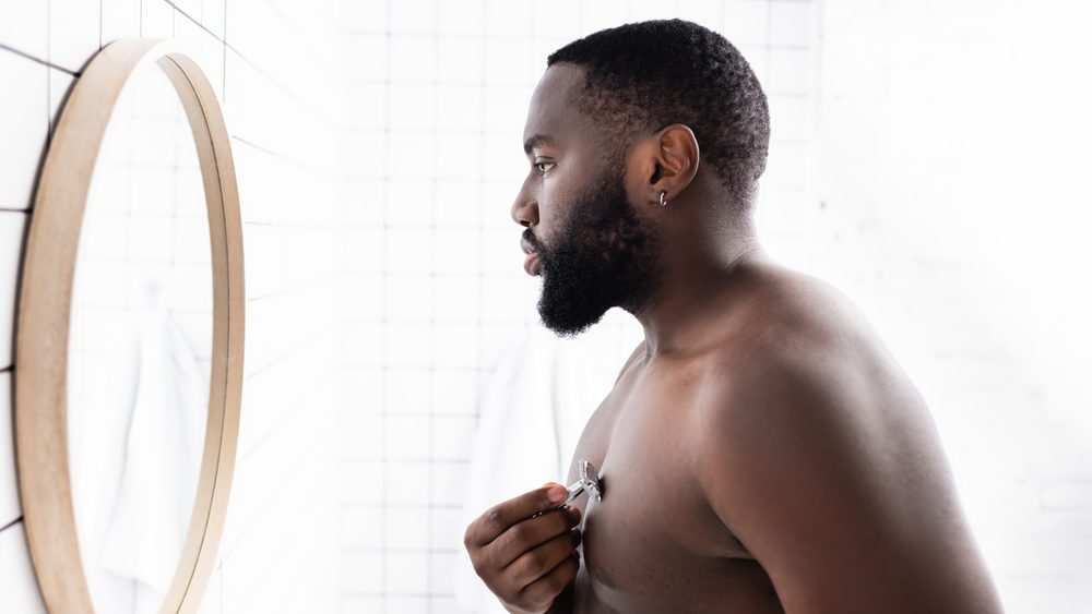 side view of afro-american man shaving chest with razor