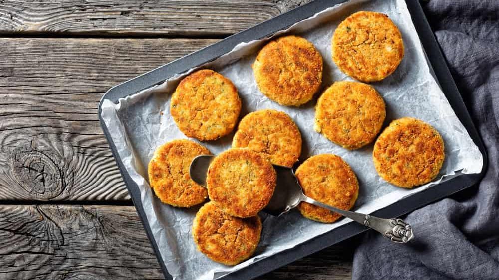 White fish cakes of white fish fillet: cod or haddock with potato and parsley, breaded in breadcrumbs and then baked in the oven, served on a sheet pan on a wooden background, top view, close-up