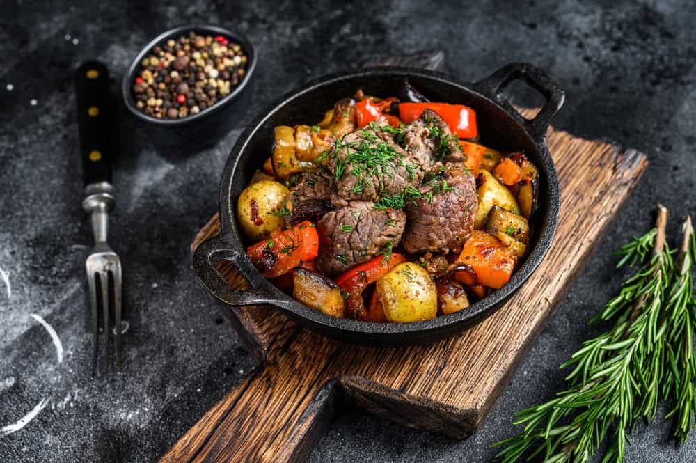 Meat stew in cooking pot on dark rustic cutting board. Black background. Top view.