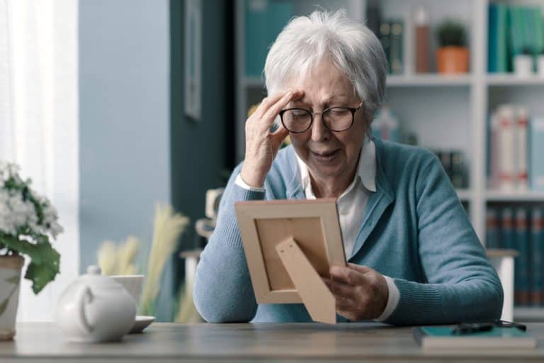 Sad senior woman mourning the loss of her husband, she is holding a picture and crying