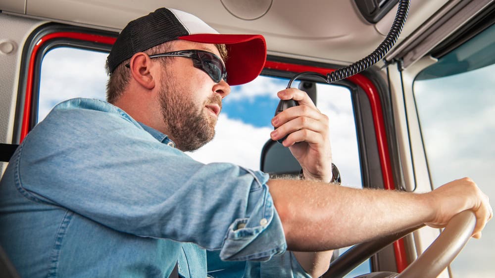 Caucasian Semi Truck Driver in His 30s Taking Conversation Using CB Radio Inside His Truck Cabin.