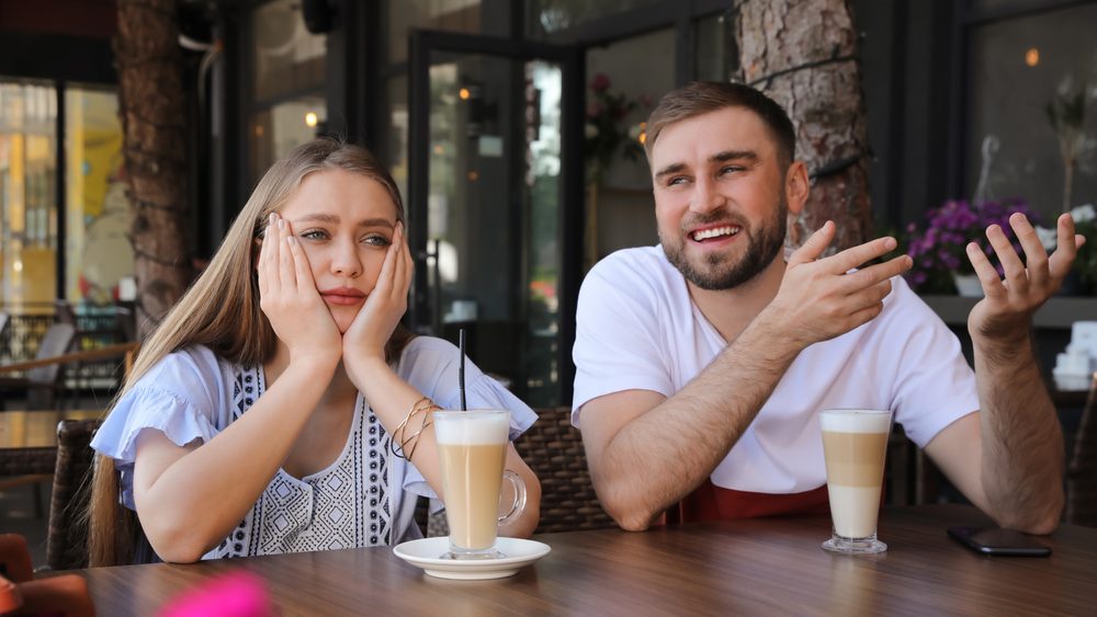 Young woman having boring date with talkative guy in outdoor cafe
