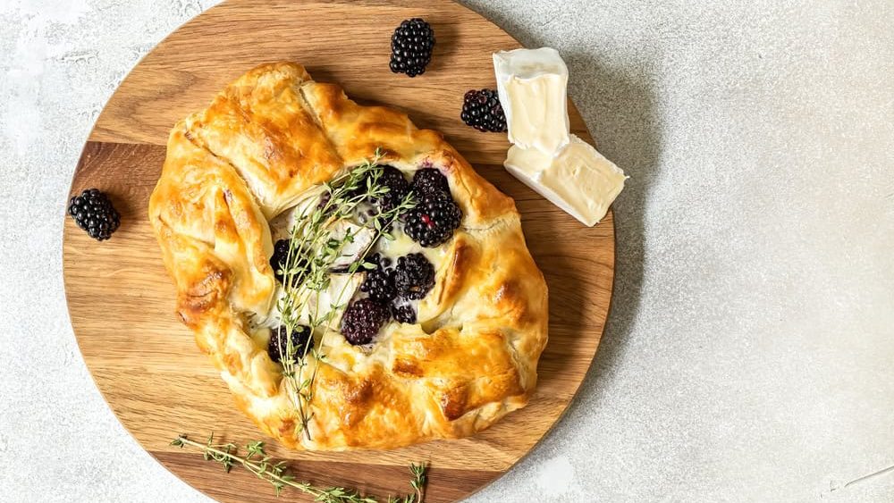 Baked brie cheese and blackberry open pie galette with thyme. Homemade puff pastry baking, sweet-savory taste, gourmet appetizer.