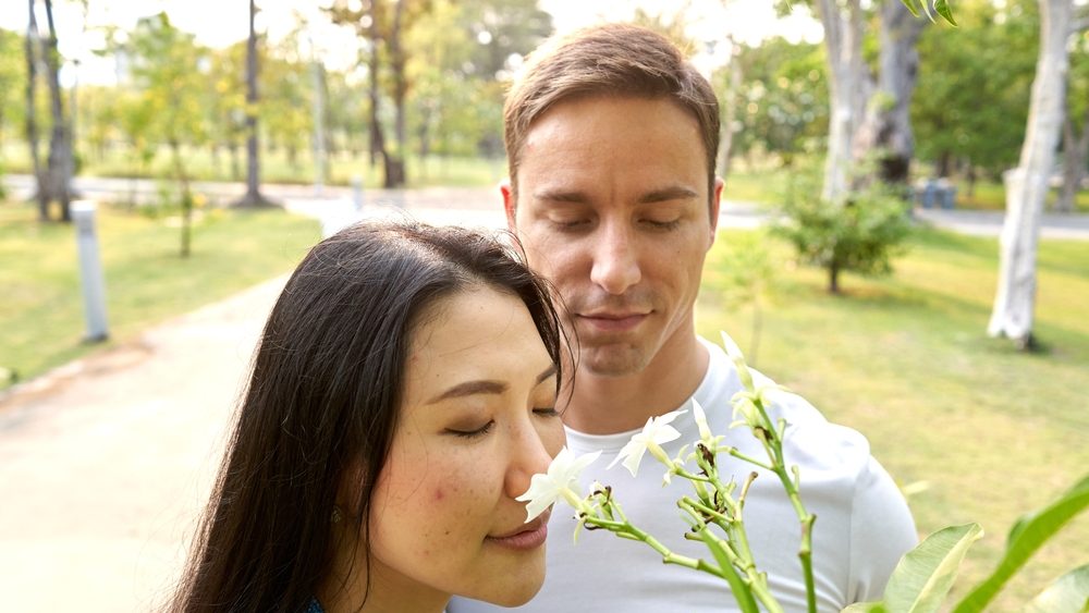 Multicultural couple smelling tropical flowers in an urban park