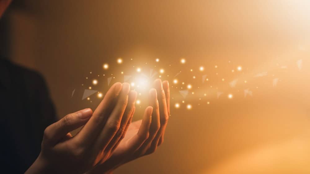 Hand praying with magic light that flows through on orange bokeh background.