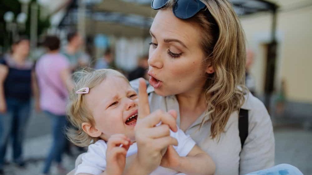 Mother scolding her little daughter in street. Child is crying and woman is shaking finger because of child's bad behavior.