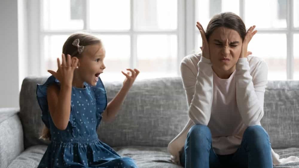 Close up upset mother covering ears, having problem with noisy naughty daughter yelling, screaming, demanding attention, frustrated mum tired of difficult child, tantrum manipulation concept