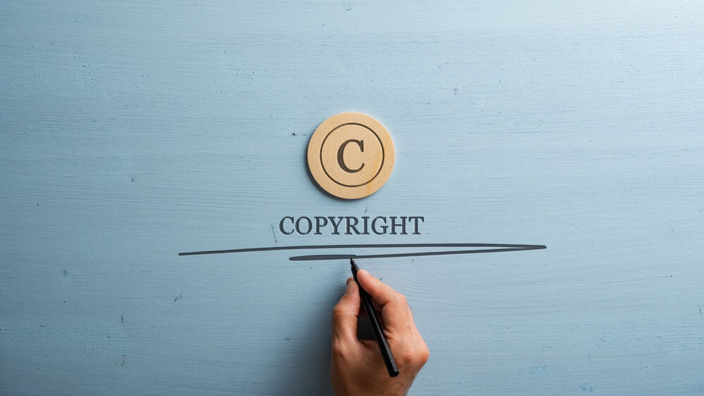 Circled letter C on a wooden cut circle with male hand writing a Copyright word under it. Over wooden blue background.